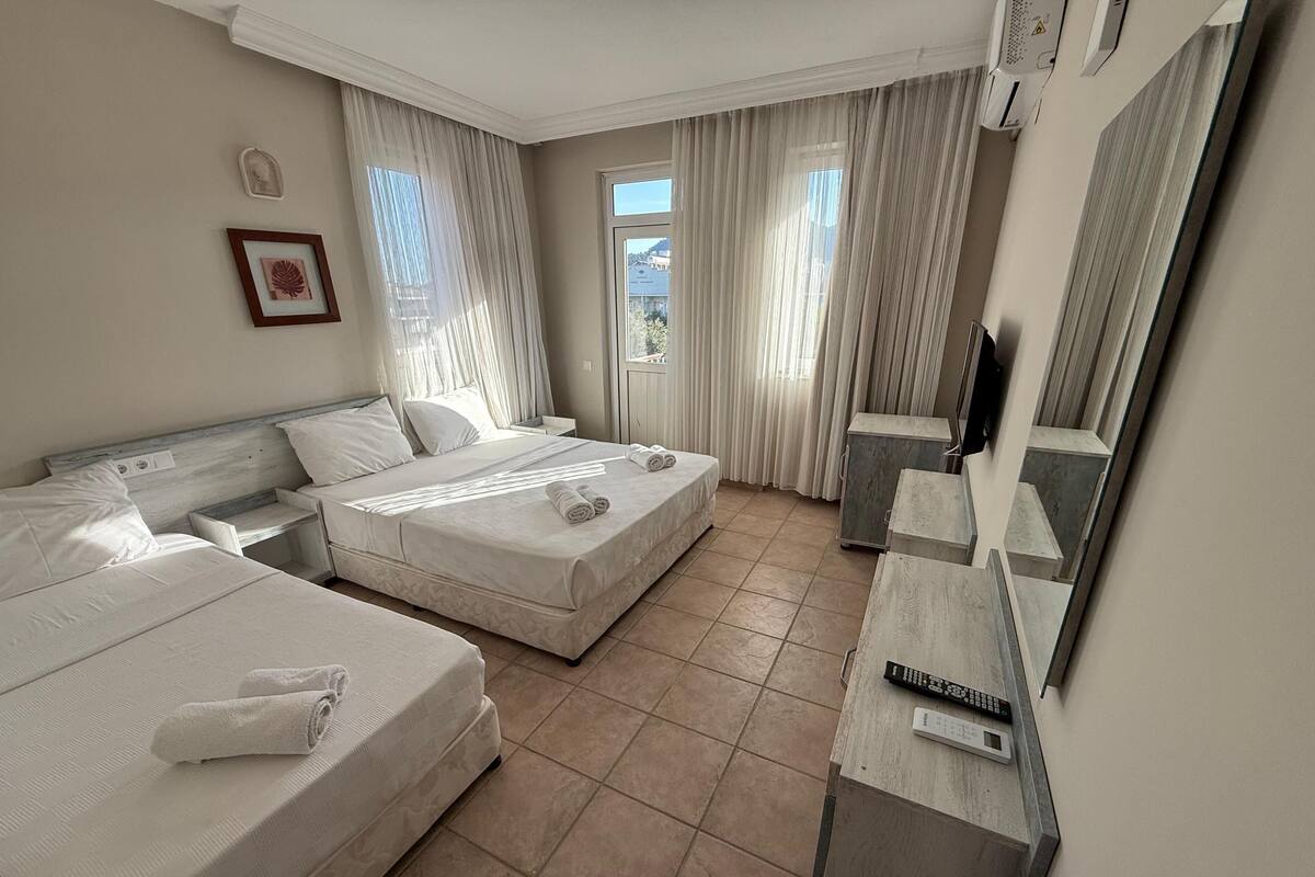 A hotel room with two beds, a TV, a minibar, and a window with curtains.