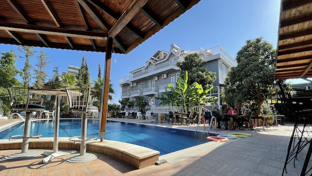 A swimming pool with a wooden deck, lounge chairs, and a covered seating area. - Tekirova Millennium Hotel (Kemer)