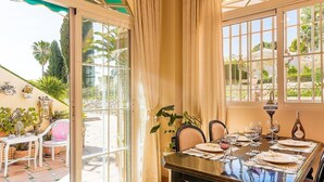 A dining area with a table set for four, a glass door leading outside, and a view of palm trees. - Apartment "Capricho Montepino 1 Las Palomas" with Pool, Wi-Fi, A/C, Terraces & Garden (La Herradura)