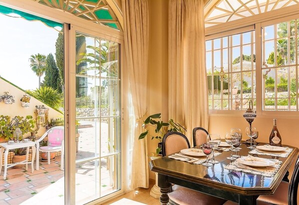 A dining area with a table set for four, a glass door leading outside, and a view of palm trees.