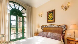 A room with a bed, a window with a green frame, a wall-mounted painting of sunflowers, and a lamp on a bedside table. - Apartment "Capricho Montepino 1 Las Palomas" with Pool, Wi-Fi, A/C, Terraces & Garden (La Herradura)