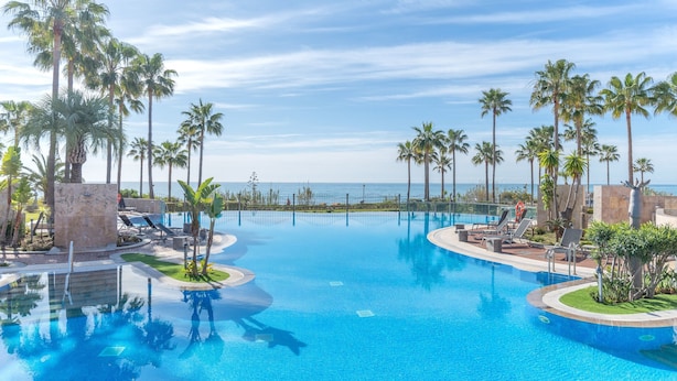 A swimming pool with palm trees, lounge chairs, and a view of the ocean. - Beach front apartment with Sea View (Estepona)