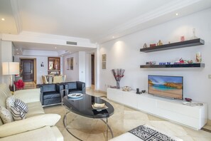 A modern living room with a sofa, a coffee table, a TV, and a dining area in the background.