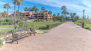 A paved walkway with a bench, palm trees, and a building in the background. - Beach front apartment with Sea View (Estepona)