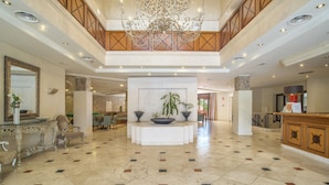 A spacious lobby with a high ceiling, a chandelier, a reception desk, and a central planter with plants. - Beach front apartment with Sea View (Estepona)
