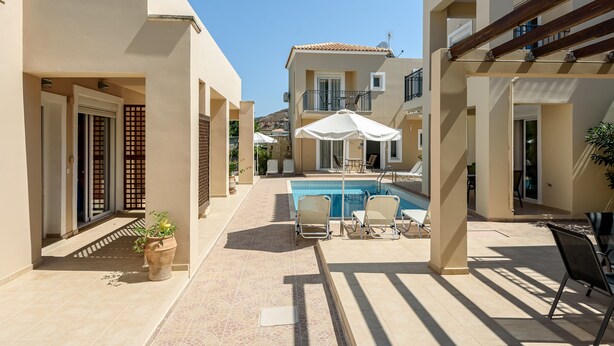 A pool area with lounge chairs and umbrellas, surrounded by buildings with balconies and a clear sky. - AZURE VILLA -BEACH FRONT  (XANIA)
