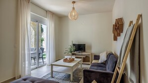 A modern living room with a sofa, a coffee table, a TV, and a sliding glass door leading to an outdoor area. - AZURE VILLA -BEACH FRONT  (XANIA)