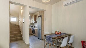 A modern kitchen with a stainless steel refrigerator, wooden cabinets, and a built-in oven. A dining table with chairs is positioned in front of the kitchen, and a staircase leads to an upper level. - AZURE VILLA -BEACH FRONT  (XANIA)