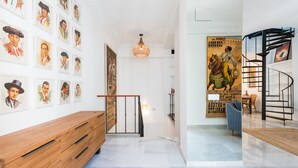 Un pasillo con un banco de madera, un muro con retratos enmarcados, un cartel grande y una escalera de caracol.