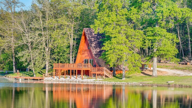 A cabin with a triangular roof, wooden deck, and a dock extending into a lake, surrounded by trees. - Lakefront A-Frame Cabin with Community Perks (Columbia)
