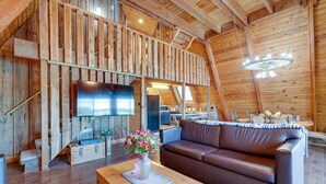 A rustic wooden interior with a brown leather sofa, a wooden coffee table with a vase of flowers, and a flat-screen TV mounted on the wall. - Lakefront A-Frame Cabin with Community Perks (Columbia)
