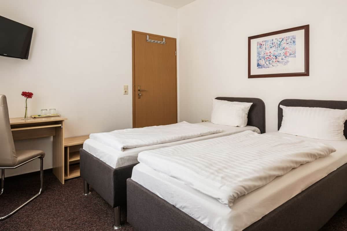 Une chambre d’hôtel avec deux lits simples, un bureau, une chaise, une télévision et une porte.