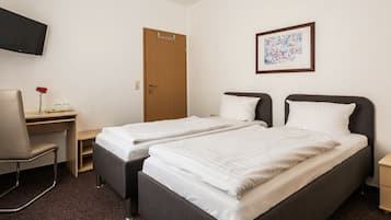 A hotel room with two single beds, a desk, a chair, a TV, and a door.