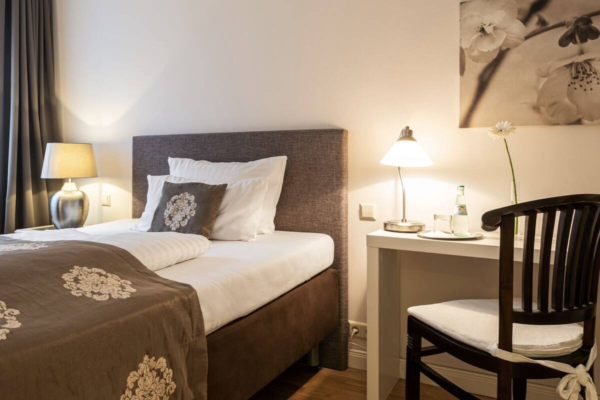 Une chambre d’hôtel comprenant un lit, une table de chevet, une lampe, une chaise et un tableau accroché au mur.