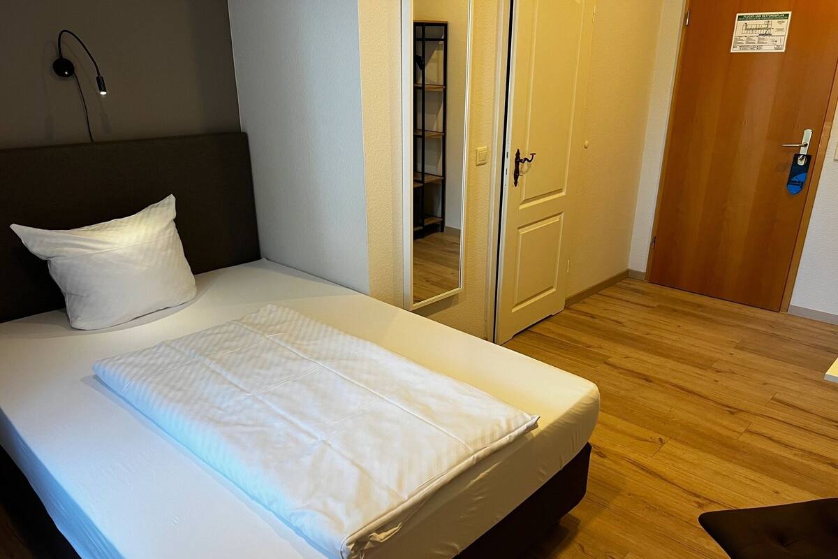 Un lit bien fait, avec du linge de lit blanc, une lampe de chevet et un plancher en bois.