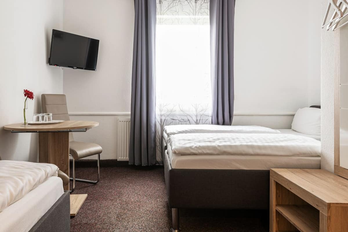 Une chambre d’hôtel comprenant un lit, un bureau avec une chaise, un téléviseur fixé au mur et une fenêtre avec des rideaux.
