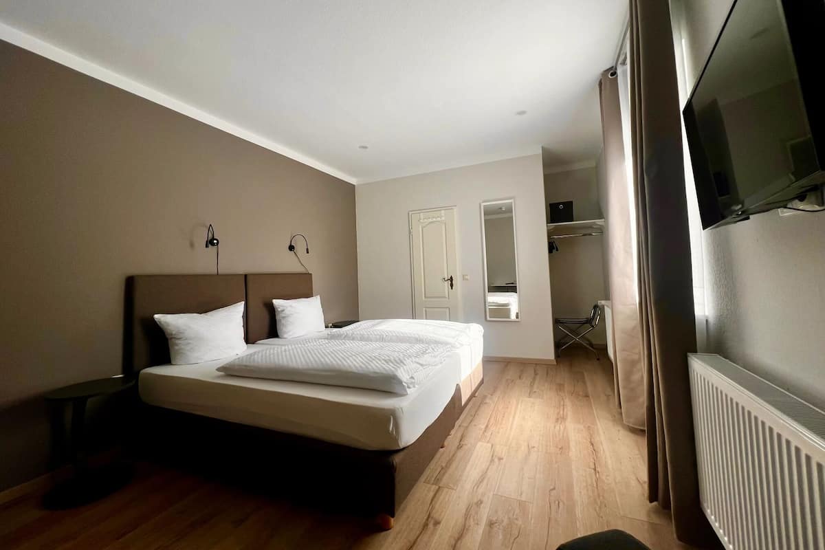 Une chambre à coucher avec un grand lit, une table de chevet, un miroir, une armoire et un téléviseur.