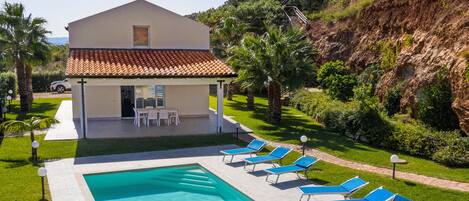 A modern house with a swimming pool, sun loungers, and a patio.