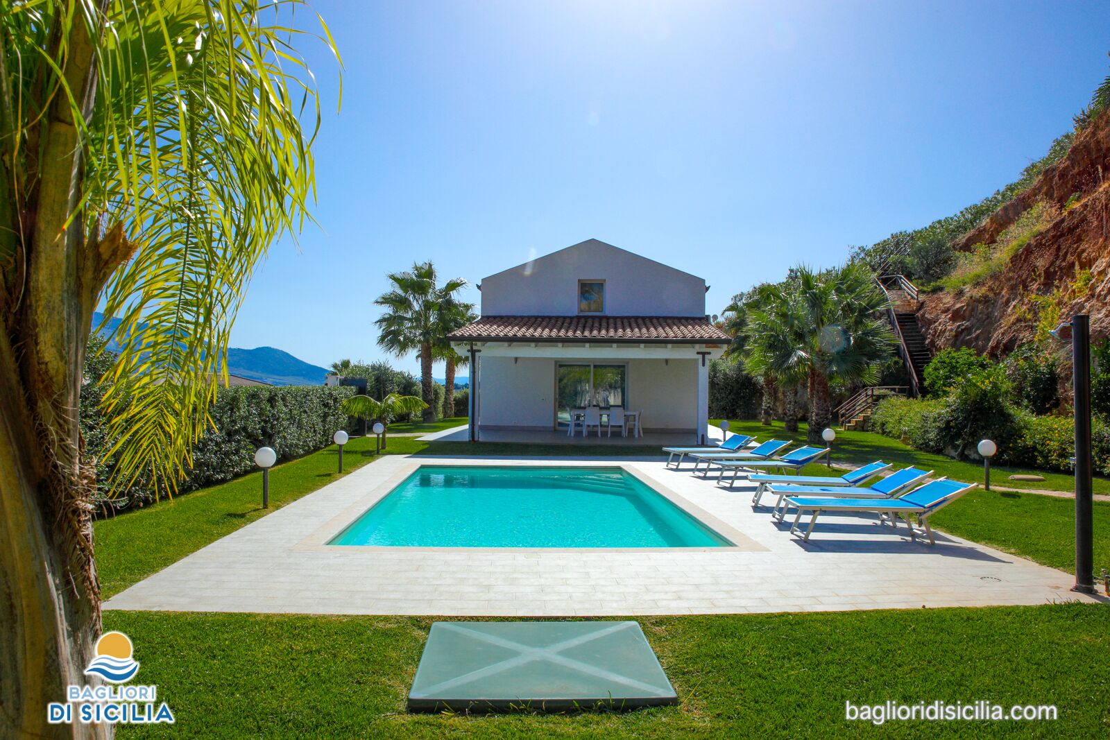 Vue sur une villa avec piscine, des chaises longues et un espace patio, le tout depuis le bord de la piscine.