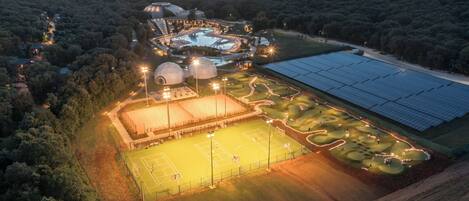 Vue aérienne d’un complexe hôtelier doté d’une piscine, de courts de tennis et de panneaux solaires.