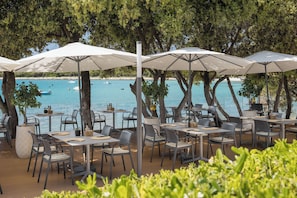 An outdoor dining area with tables and chairs, umbrellas, and a view of the sea.