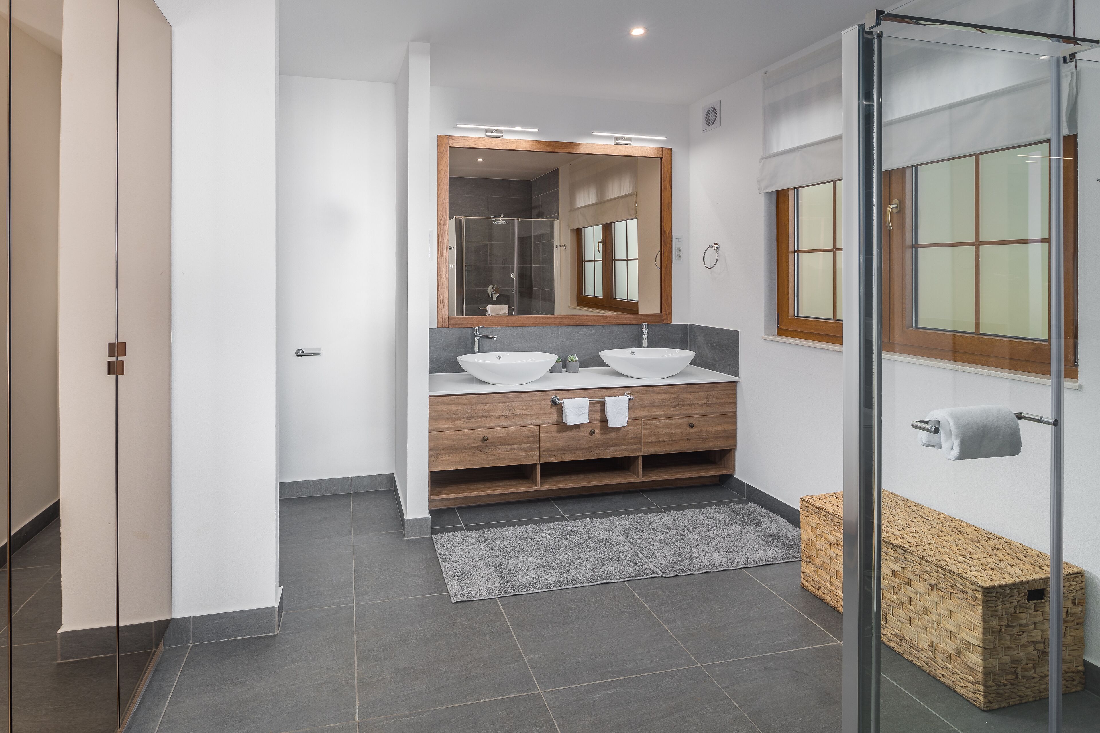 A modern bathroom with two sinks, a large mirror, and a glass shower enclosure.