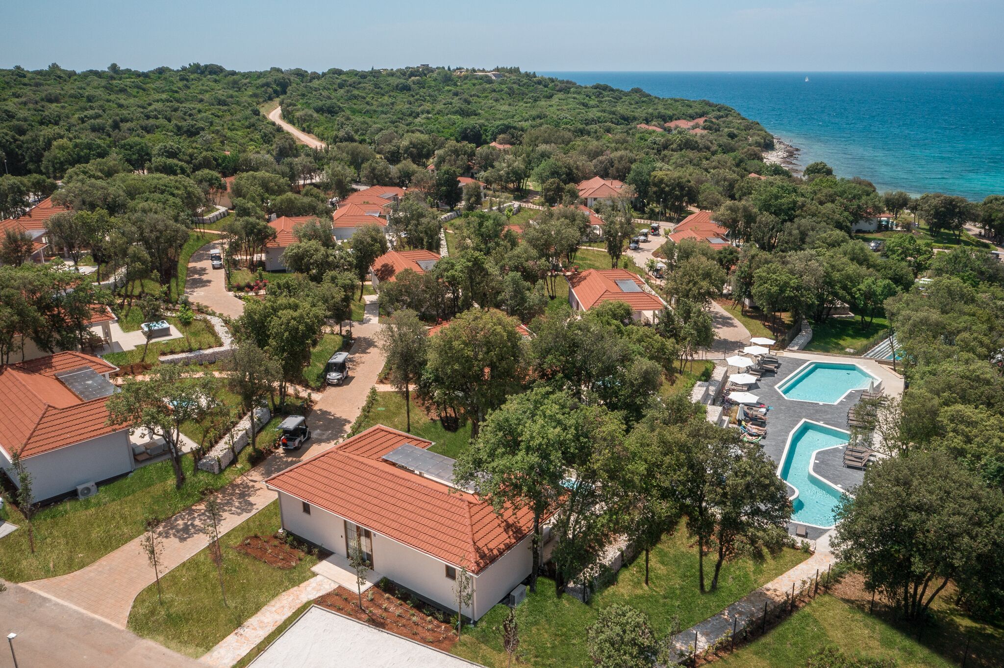 Vista aérea de una zona residencial con casas, piscina y costa.