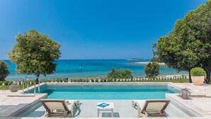 A swimming pool with lounge chairs and a table, overlooking a beach and the sea. - Luxury Beach Villas Porto Bus (Bale)