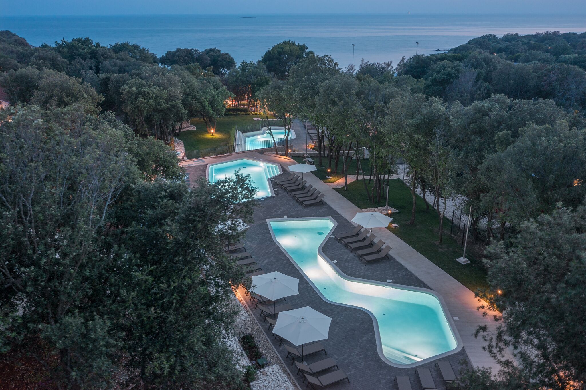 Vista aérea de un resort con varias piscinas, zonas de descanso y un entorno boscoso.