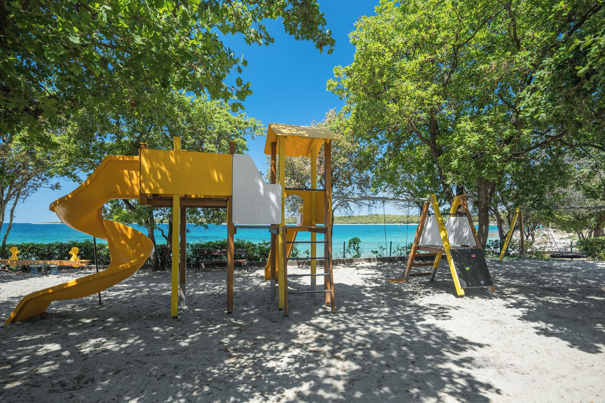 A beachside art installation with a yellow spiral structure and a white chair.