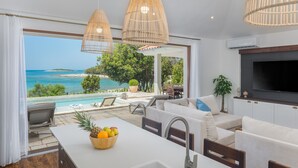 A modern kitchen with a view of the sea, a dining area with a white table, and a cozy seating area with a TV. - Luxury Beach Villas Porto Bus (Bale)