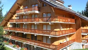 Un chalet en bois à plusieurs étages, doté de balcons, d’une fondation en pierre et d’un toit en pente.