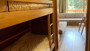 Une chambre avec un lit superposé, un canapé et un fauteuil, un plancher en bois et une vue par la fenêtre.