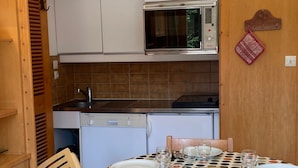 Une cuisine compacte équipée d’un four à micro-ondes, d’un évier et d’un lave-vaisselle. Une table à manger est dressée, avec des assiettes et des verres.