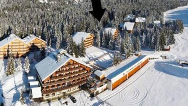 Un chalet doté de plusieurs cabanes en rondins, d'un télésiège et surplombant un paysage montagneux enneigé.