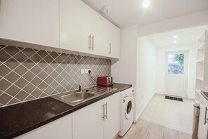 A modern kitchen with white cabinets, a black countertop, a built-in washing machine, and a window with a view.