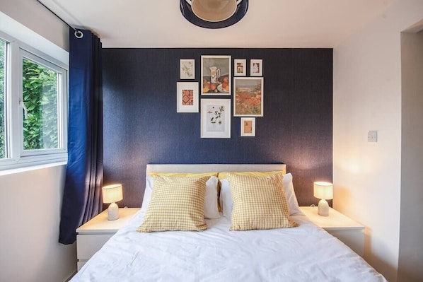 A hotel room with a bed, two bedside tables, a window with curtains, and a wall with framed pictures.
