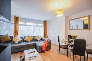A modern living room with a sofa, coffee table, dining table with chairs, and a large window with curtains.