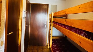 A narrow hallway with wooden bunk beds on one side and a closed door at the end.