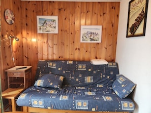 A wooden-paneled room with a sofa, a small table, a lamp, and two framed pictures on the wall. - Cozy apartment in Morillon, pets allowed (Morillon Village)