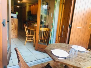 A wooden dining table with chairs, a glass door leading to a kitchen, and a bench.