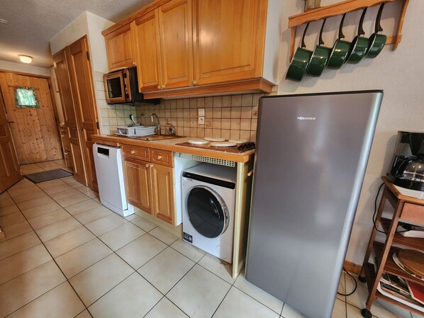 A kitchen with wooden cabinets, a microwave, a washing machine, a refrigerator, and a coffee maker. - Cozy apartment in Morillon, pets allowed (Morillon Village)