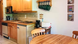Cucina con mobili in legno, forno a microonde, fornello e macchina per il caffè. Presente un tavolo da pranzo con sedie e una piccola mensola con oggetti decorativi.