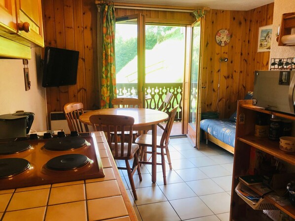 A cozy kitchen with a dining table and chairs, a small TV, and a bookshelf. - Cozy apartment in Morillon, pets allowed (Morillon Village)