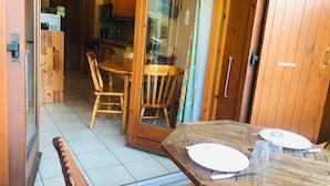 Un tavolo da pranzo in legno con sedie, una porta vetrata che dà su una cucina e una panca.