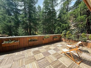 A wooden deck with a herringbone pattern, surrounded by a wooden railing with planters, overlooking a forested area.