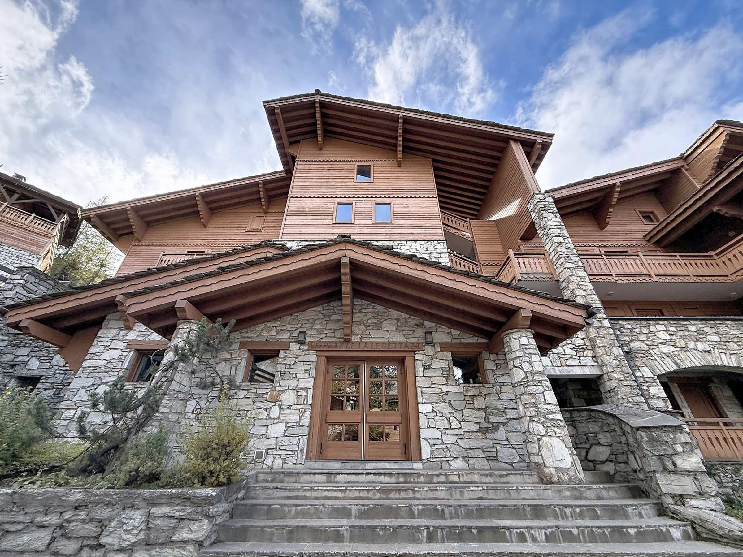 A traditional stone building with a wooden facade, a central entrance with a double door, and a sloped roof.