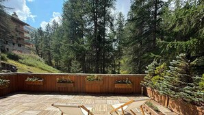 Une terrasse en bois avec deux chaises longues, entourée d’une clôture en bois et d’une forêt dense.