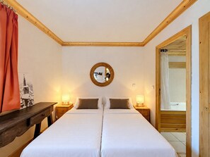 A double bed with two nightstands, a round mirror, and a wooden door leading to a bathroom. - Charming 4-room apartment for 6 at slopes' edge with wifi (Val-d'Isère)