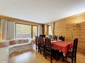 A room with a dining table set for four, a sofa, and a view of a balcony.